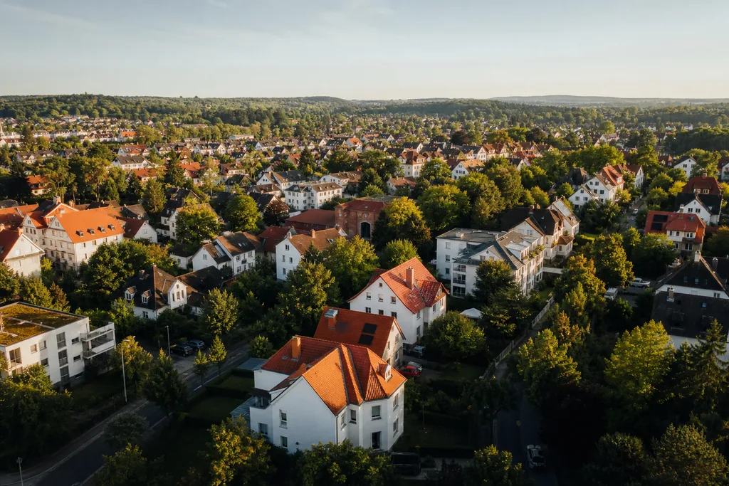 Luftaufnahme einer typischen deutschen Wohnstadt mit roten Ziegeldächern und viel Grün an einem sonnigen Tag.