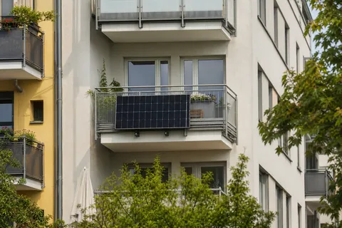 Symbolbild zum Ratgeber „Balkonkraftwerk zur Miete: Was Vermieter noch verbieten dürfen“: die Fassade eines Mehrfamilienhauses mit einem Balkonkraftwerk an einem der Balkone.
