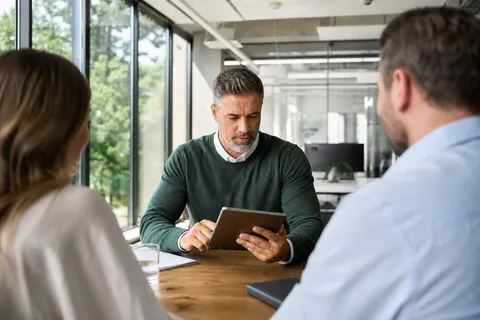 Symbolbild zum Ratgeber „Gewerbestrom vergleichen: die wichtigsten Kriterien“: eine Unternehmerin vergleicht Tarife auf dem Tablet am Besprechungstisch.